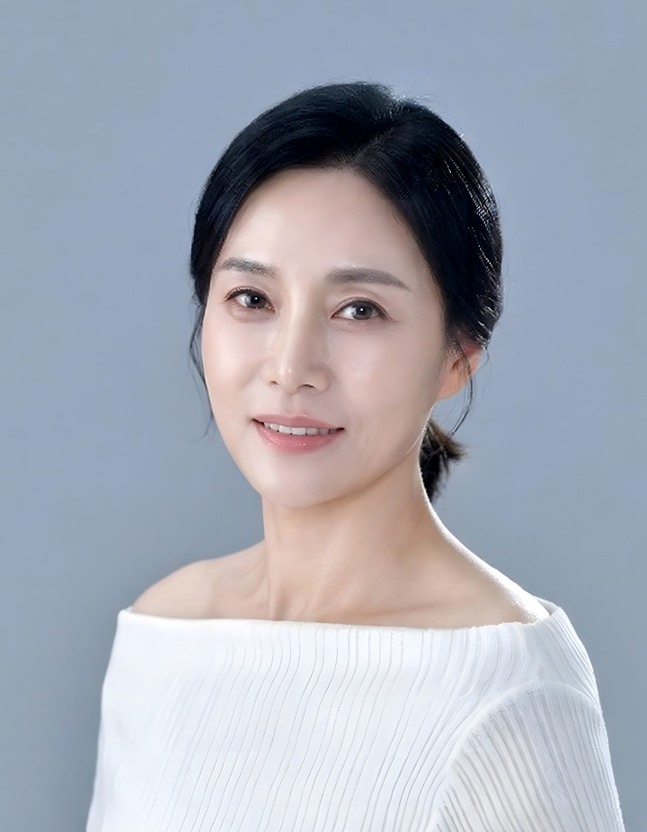 흰색 오프숄더 상의를 입은 여성의 세미프로필사진. 은은한 블루그레이 배경에서 단정하게 묶은 헤어스타일과 부드러운 미소로 우아하고 세련된 분위기를 표현한 인물사진.
